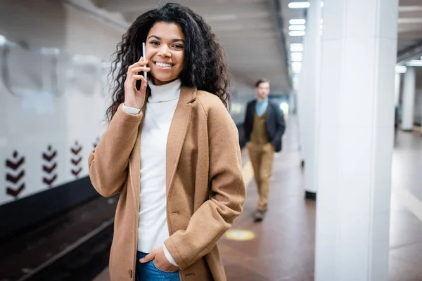 Felice donna afroamericana che parla su smartphone vicino all'uomo in metropolitana su sfondo sfocato — Foto stock
