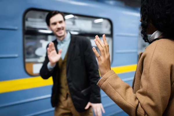 Femme afro-américaine et homme agitant les mains près du wagon dans le métro sur fond flou — Photo de stock
