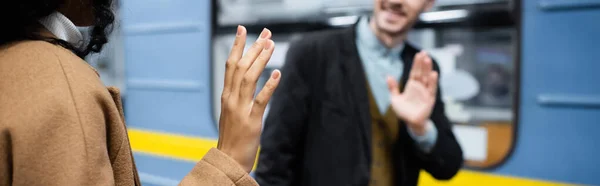 Vista parziale di felice coppia interrazziale agitando le mani vicino al carro in metropolitana, banner — Foto stock