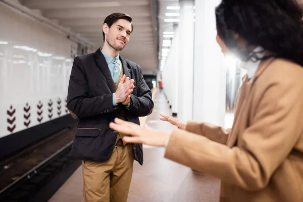 Uomo in piedi con le mani in preghiera e guardando la donna afro-americana su sfondo sfocato — Foto stock