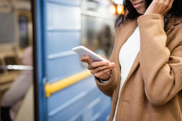 Vista ritagliata di donna afro-americana utilizzando smartphone vicino carro in metropolitana su sfondo sfocato — Foto stock