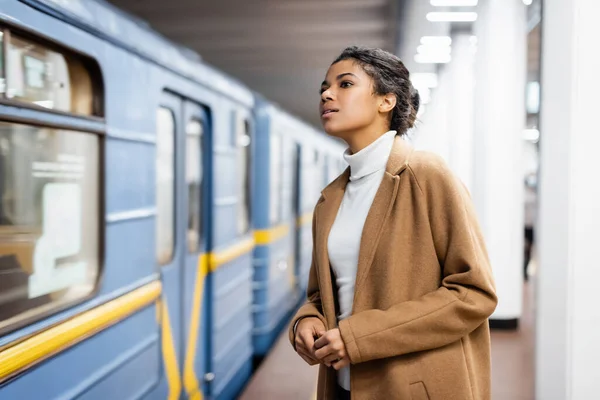 Кучерява афроамериканська жінка дивиться на вагон метро на розмитому фоні — стокове фото