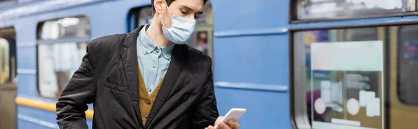 Homem em máscara médica segurando smartphone perto de vagão de metro, banner — Fotografia de Stock