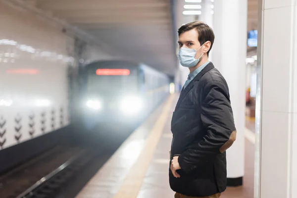 Uomo in maschera medica in piedi con mano in tasca vicino al carro della metropolitana — Foto stock