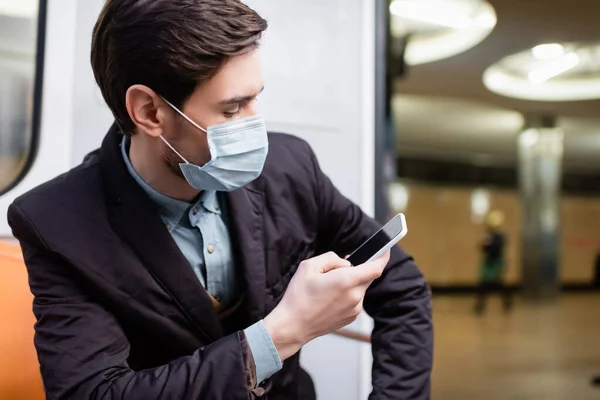 Людина в медичній масці, використовуючи смартфон у вагоні метро — стокове фото