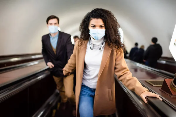 Interrazziale uomo e donna in maschere mediche su scala mobile in metropolitana — Foto stock
