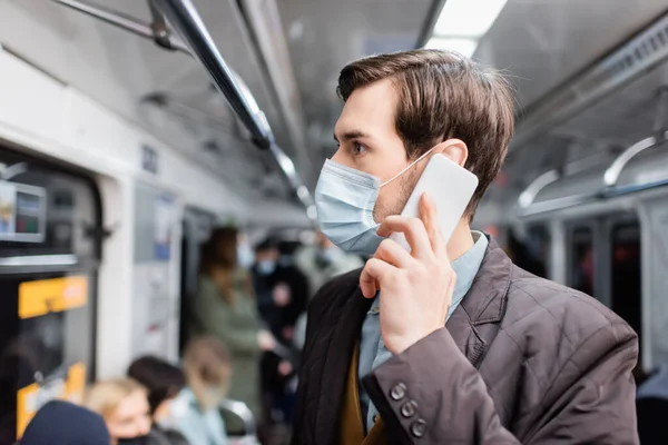 Homem em máscara médica falando no smartphone enquanto em pé no vagão do metro — Fotografia de Stock