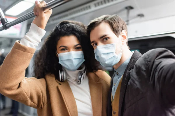 Multikulturelles Paar in medizinischen Masken im Waggon der U-Bahn — Stockfoto