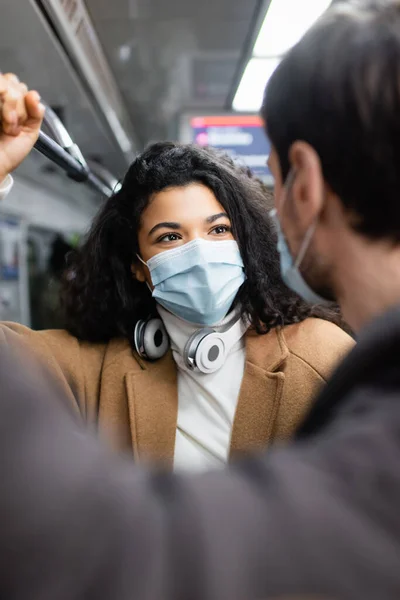 Femme afro-américaine et homme aux masques médicaux se regardant dans un wagon de métro — Photo de stock
