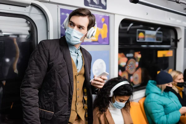 Мужчина держит смартфон рядом с африканской американкой в медицинской маске на размытом фоне — стоковое фото