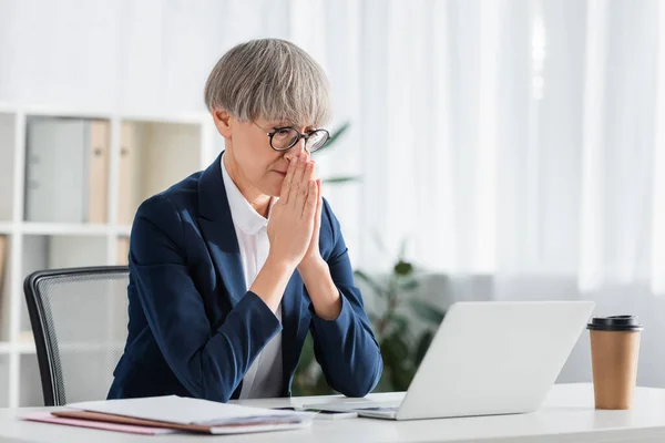 Líder del equipo preocupado en gafas con las manos orantes mirando el portátil en el escritorio — Stock Photo