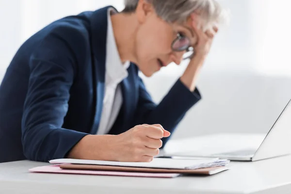 Blurred middle aged businesswoman with clenched fist suffering from headache in office — Stock Photo