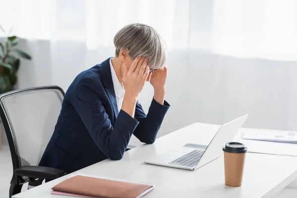 Mujer de negocios agotada y de mediana edad que sufre de dolor de cabeza en el cargo - foto de stock