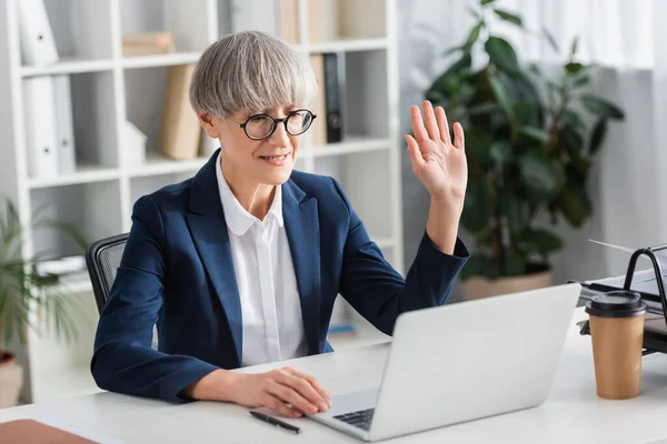 Middle aged team leader in glasses waving hand during video call — Stock Photo