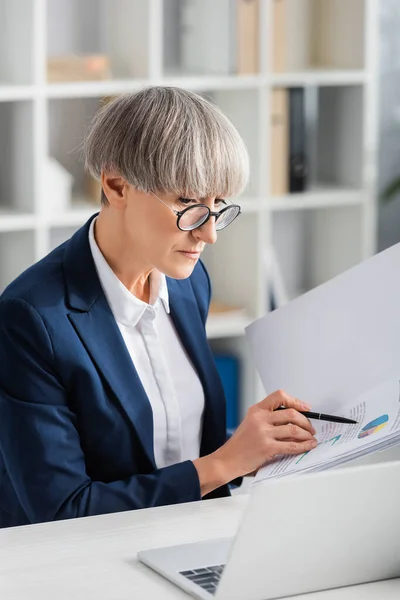 Middle aged team leader in glasses holding folder with charts and graphs — Stock Photo