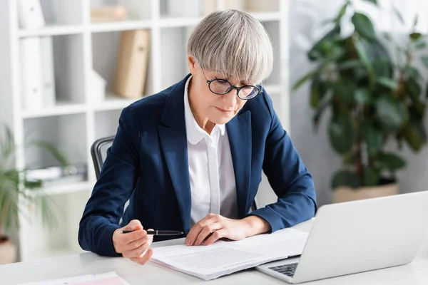 Teamleiter mittleren Alters in Brille mit Stift in der Nähe von Dokumenten auf dem Schreibtisch — Stockfoto