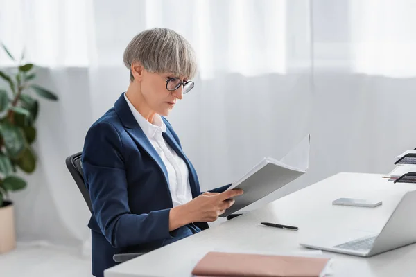 Middle aged team leader in glasses looking at folder with documents — Stock Photo