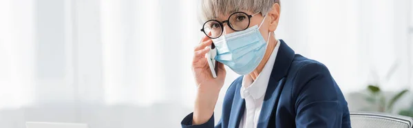 Middle aged team leader in glasses and medical mask talking on smartphone, banner — Stock Photo