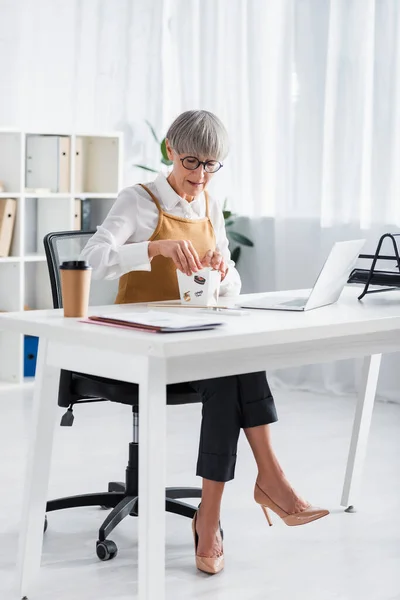 Mature team leader looking at takeaway lunch in carton box on desk — Stock Photo