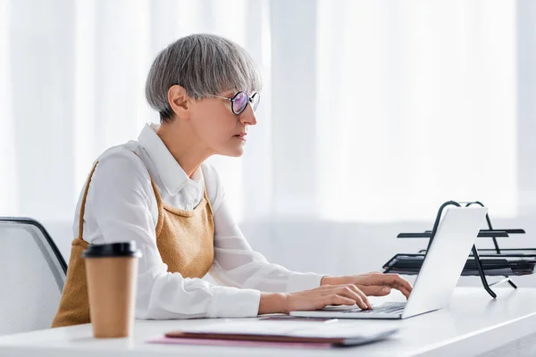 Mature chef d'équipe dans les lunettes en utilisant ordinateur portable sur le bureau — Photo de stock