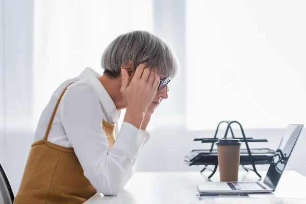 Vue latérale du chef d'équipe mature regardant l'ordinateur portable dans le bureau — Photo de stock