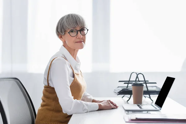 Mature team leader sitting at desk and looking at camera in office — Stock Photo