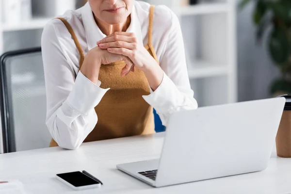 Cropped view of mature team leader sitting at desk with gadgets — Stock Photo