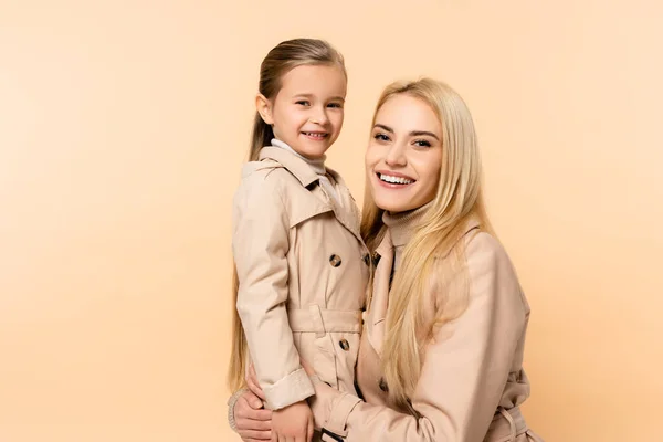 Alegre rubia madre abrazando feliz hija aislado en beige - foto de stock