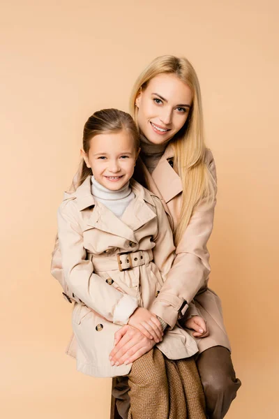 Alegre rubia madre abrazando feliz hija aislado en beige - foto de stock