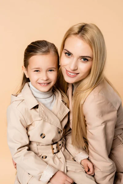 Fröhliche blonde Mutter und glückliche Tochter schauen vereinzelt in die Kamera auf beige — Stockfoto