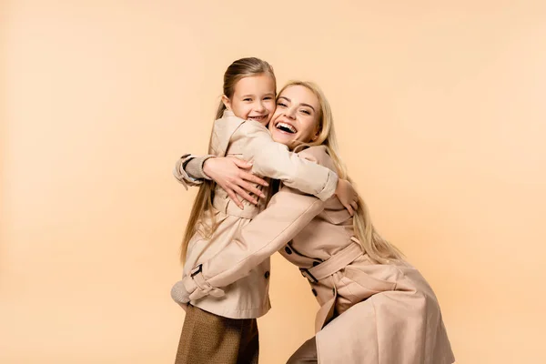 Niño feliz abrazando madre rubia sorprendida aislada en beige - foto de stock