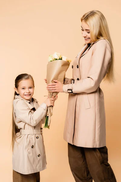 Cheerful kid giving flowers to happy mother on 8 march isolated on beige — Stock Photo