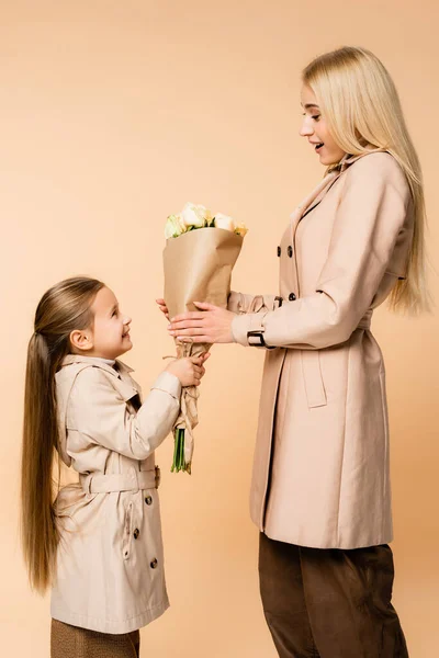 Seitenansicht eines fröhlichen Kindes, das der überraschten Mutter am 8. März Blumen schenkt, isoliert auf beige — Stockfoto