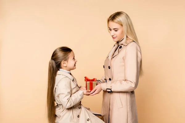 Cheerful kid giving present to happy mother on 8 march isolated on beige — Stock Photo