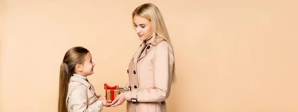 Enfant joyeux donnant cadeau à la mère heureuse sur 8 mars isolé sur beige, bannière — Photo de stock