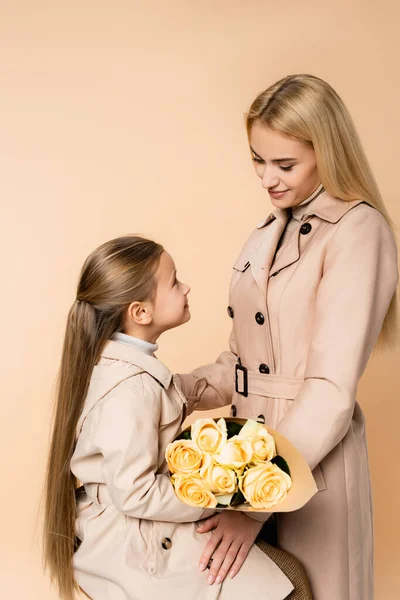 Niño alegre sosteniendo rosas cerca de la madre el 8 de marzo aislado en beige - foto de stock