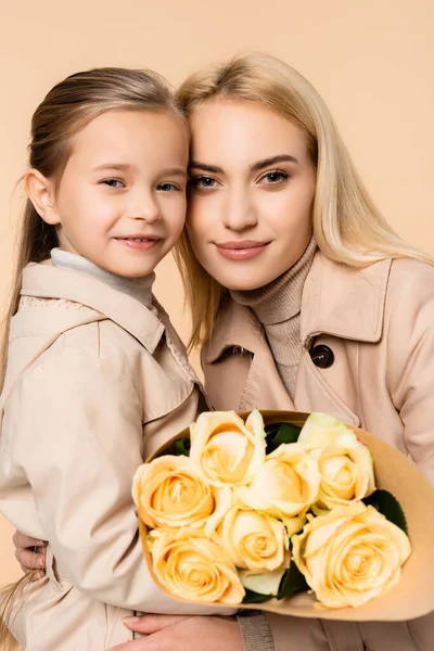 Fröhliches Kind mit Rosen neben fröhlicher Mutter am 8. März isoliert auf beige — Stockfoto