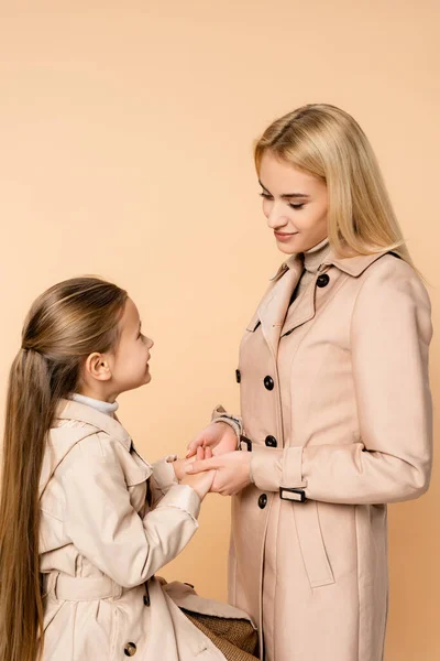 Madre e hija cogidas de la mano y se miran aisladas en beige - foto de stock