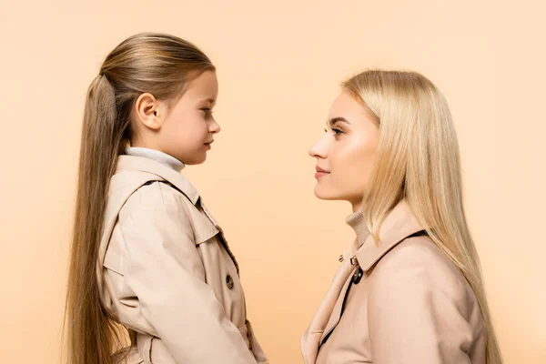 Vista lateral de la madre y la hija mirándose aisladas en beige - foto de stock