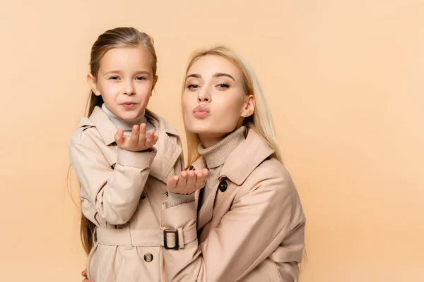 Mère et fille en manteaux envoyant des baisers d'air isolés sur beige — Photo de stock