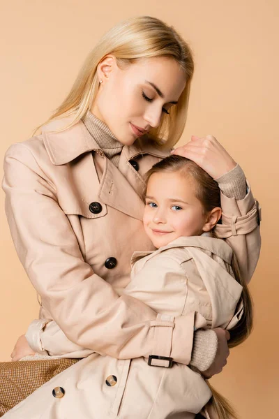 Cuidado y madre rubia abrazando hija aislada en beige - foto de stock