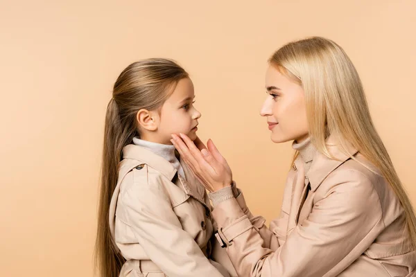 Vue latérale de la mère attentionnée touchant le visage de la fille isolée sur beige — Photo de stock