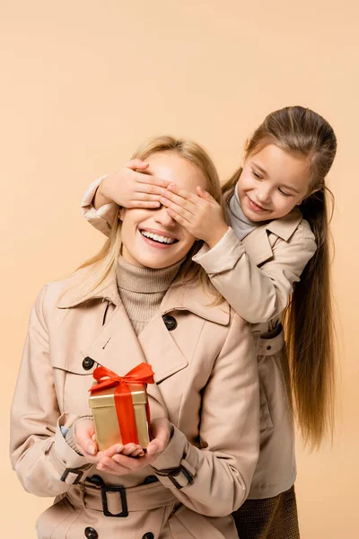 Enfant couvrant les yeux d'une mère heureuse avec présent isolé sur beige — Photo de stock