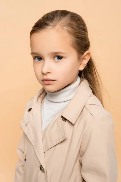 Kid in trench coat looking at camera isolated on beige — Stock Photo