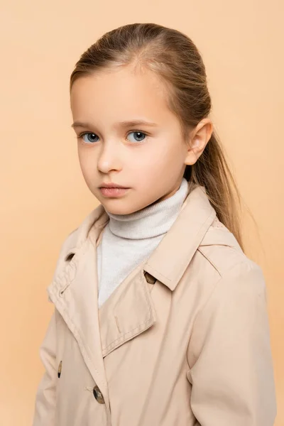 Niño en gabardina mirando a la cámara aislada en beige - foto de stock