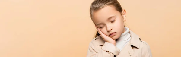 Niño somnoliento con los ojos cerrados en gabardina aislado en beige, pancarta - foto de stock