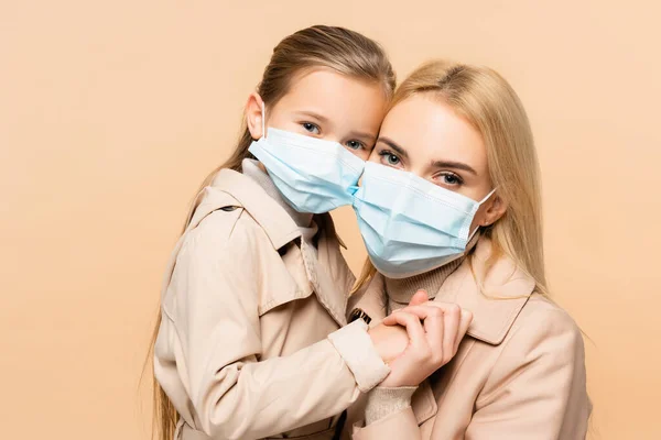 Mother and daughter in medical masks holding hands isolated on beige — Stock Photo