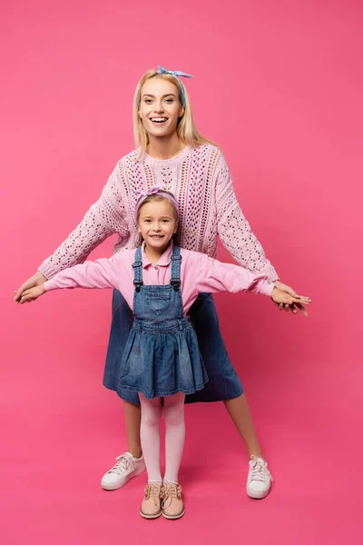 Comprimento total da mãe e da criança sorrindo e de pé com as mãos estendidas isoladas no rosa — Fotografia de Stock