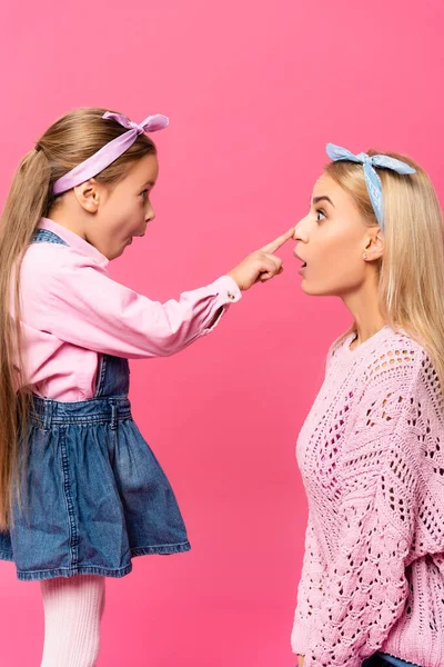 Seitenansicht des überraschten Kindes berührt Nase der Mutter isoliert auf rosa — Stockfoto