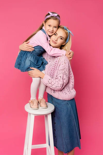 Heureux enfant debout sur chaise et étreignant mère sur rose — Photo de stock